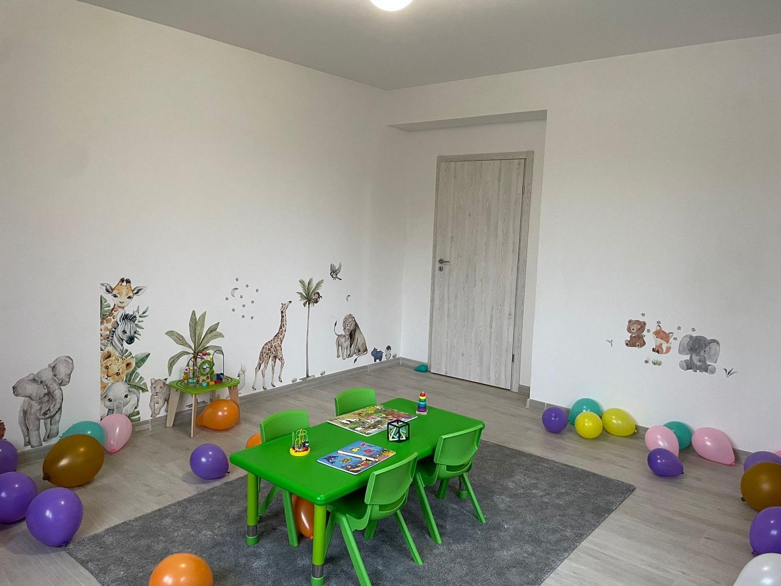 Sală de grupă cu animăluțe pictate pe perete și masă verde